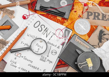 Espace de travail créatif sur le thème OSINT avec des outils vintage, des notes manuscrites et des éléments de presse sur une table grunge. Accessoires thématiques, plat, vue de dessus Banque D'Images