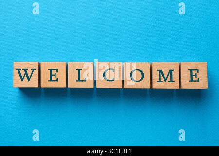 Word Welcome fait de cubes en bois sur fond bleu clair, vue de dessus Banque D'Images