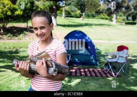 Fille portant des bûches de bois de chauffage debout sur une couverture dans le parc près de la tente de camping, espace de copie Banque D'Images