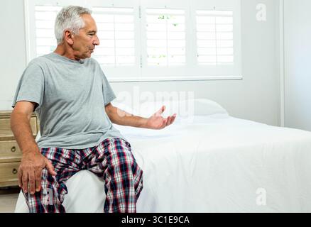 Lit reposant sous des volets ouverts dans une chambre grise bien rangée avec table de chevet en bois Banque D'Images