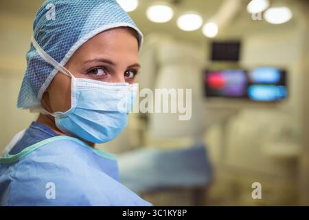 Chirurgien féminin portant un chapeau de gommage ou un masque ou une blouse sous des lumières chirurgicales, surveille le flou de l'équipement Banque D'Images