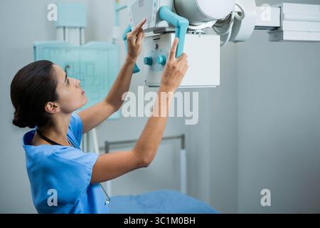 Technicien radiologique féminin dans les frotteurs ajustant les rayons X contrôle le panneau dans la salle d'imagerie, espace de copie Banque D'Images
