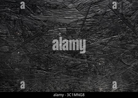 Texture de contreplaqué noir. Surface texturée rugueuse d'un panneau de particules peint en noir. Fond en aggloméré noir. Gros plan. Mur présentant des fissures visibles. Banque D'Images