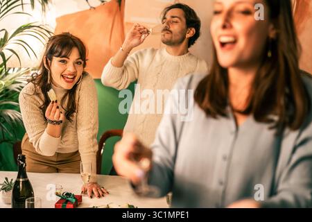 Une belle jeune femme sourit à la caméra tout en mangeant un apéritif, tandis que ses amis boivent du champagne et rient en arrière-plan pendant un Christ amusant Banque D'Images