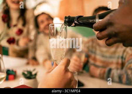 Plan macro détaillé de champagne pétillant versé dans une flûte en verre élégante, avec les visages souriants flous d'amis en fête Banque D'Images