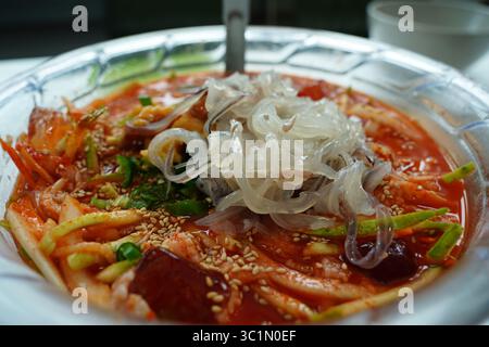 Soupe épicée de nouilles froides aux fruits de mer coréens (Mulhoe) avec sashimi de calmars frais dans un grand bol Banque D'Images