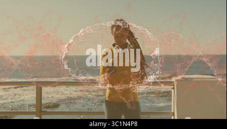 Penchée sur la balustrade, femme portant une chemise moutarde tenant un smartphone à la promenade, portant des écouteurs Banque D'Images