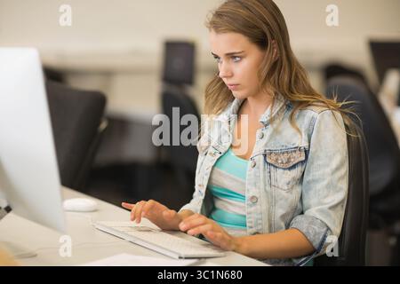 Femme tapant sur le clavier externe au poste de travail de laboratoire informatique portant une veste en denim et un haut rayé Banque D'Images