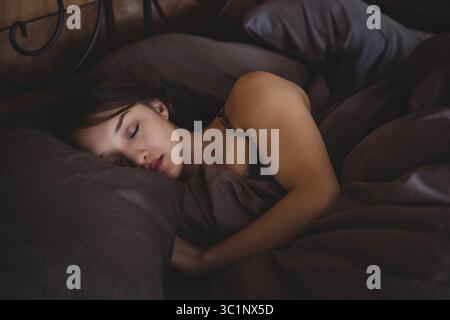 Femme asiatique endormie couchée sur le côté dans la chambre par tête de lit en fer forgé avec literie gris foncé Banque D'Images