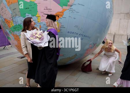 Les Graduands célèbrent l'obtention de leur diplôme de la London School of Economics (LSE) devant un globe inversé, une sculpture de l'artiste Mark Wallinger, lauréat du prix Turner, intitulée 'The World Turned Upside Down', le 22 juillet 2025, à Londres, en Angleterre. Banque D'Images