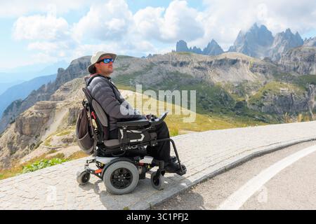 L'homme handicapé en fauteuil roulant explore la beauté des Dolomites en Italie. Il admire les montagnes à couper le souffle tout en se prélassant dans le Banque D'Images