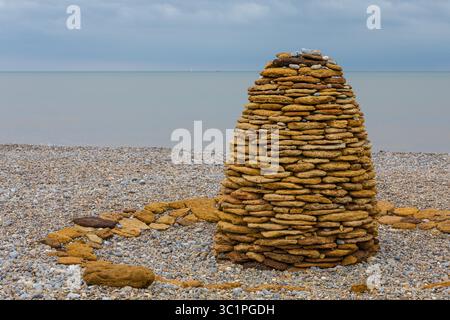 Un cairn en forme de ruche fait de pierres empilées sur une plage de galets, mêlant matériaux naturels et expression artistique sur la côte britannique. Banque D'Images