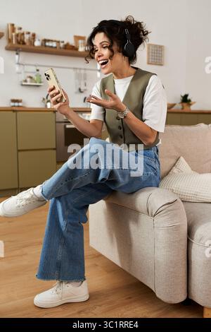 Une jeune femme joyeuse étudie à la maison, s'engageant joyeusement avec son téléphone. Banque D'Images