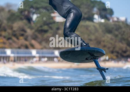 Gros plan d'un homme dans une combinaison noire surfe les vagues à l'aide d'une planche de surf hydrofoil électrique. Banque D'Images