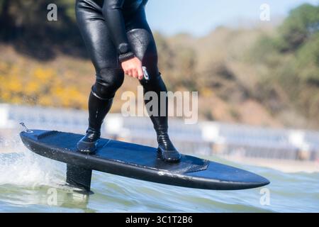 Gros plan d'un homme dans une combinaison noire surfe les vagues à l'aide d'une planche de surf hydrofoil électrique. Banque D'Images
