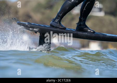 Gros plan d'un homme dans une combinaison noire surfe les vagues à l'aide d'une planche de surf hydrofoil électrique. Banque D'Images