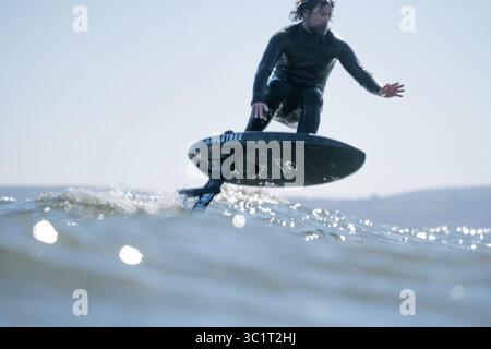 Un homme en combinaison noire surfe les vagues à l'aide d'une planche de surf hydrofoil électrique. Banque D'Images