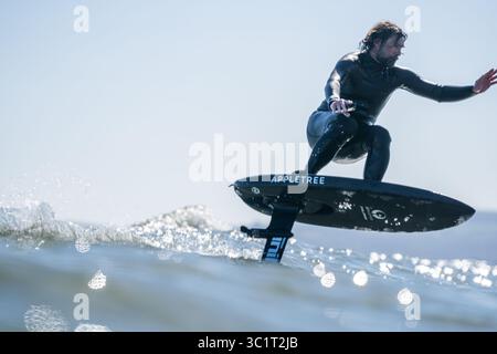 Un homme en combinaison noire surfe les vagues à l'aide d'une planche de surf hydrofoil électrique. Banque D'Images
