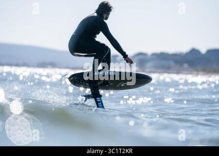 Un homme en combinaison noire surfe les vagues à l'aide d'une planche de surf hydrofoil électrique. Banque D'Images