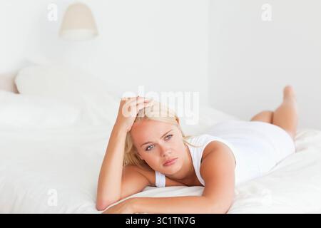 Femme portant haut couché sur le lit soutenant les avant-bras sur l'oreiller à côté de la lampe regardant latéralement dans la chambre Banque D'Images