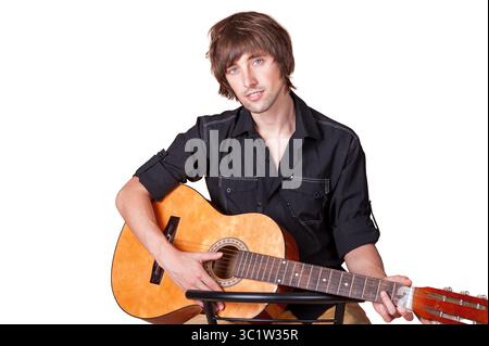 Un homme tape sa guitare avec la mise au point dans un espace de studio lumineux et simple. Banque D'Images