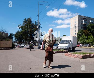 Kiev, Ukraine - 20 juillet 2025 : femme âgée marchant sur le trottoir de la ville pendant une journée d'été ensoleillée, avec des bâtiments, des arbres et une camionnette blanche en arrière-plan Banque D'Images