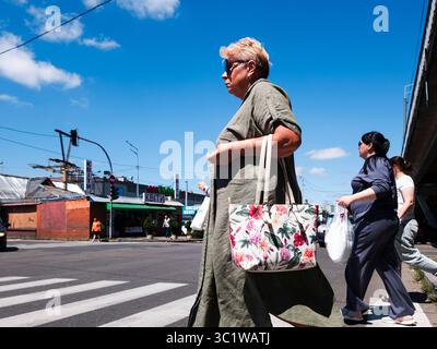 Kiev, Ukraine - 20 juillet 2025 : des gens traversent une rue en été près d'un magasin de fleurs, avec une femme avec des lunettes de soleil et un sac floral au premier plan, des voitures qui passent et un ciel bleu avec quelques nuages Banque D'Images