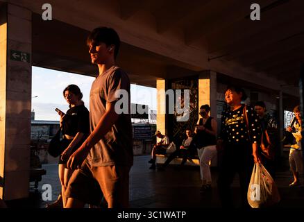 Kiev, Ukraine - 20 juillet 2025 : les gens marchent et utilisent leur smartphone dans une gare au coucher du soleil, créant une scène dynamique et évocatrice de la vie urbaine Banque D'Images