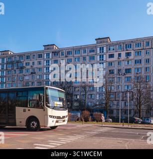 Kiev, Ukraine - 20 juillet 2025 : bus blanc conduisant sur un passage piétonnier devant un grand immeuble usé de l'ère soviétique, par une journée ensoleillée Banque D'Images