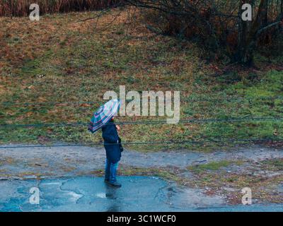 Kiev, Ukraine - 20 juillet 2025 : homme avec parapluie marchant près du chemin de fer pendant le jour pluvieux d'automne, concept de solitude et de mélancolie dans la ville Banque D'Images