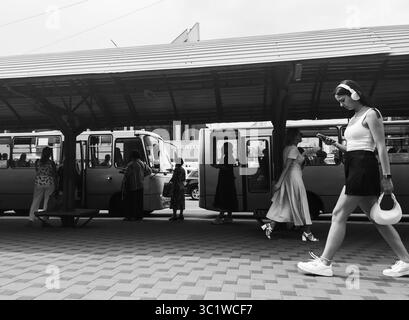 Kiev, Ukraine - 20 juillet 2025 : photographie de rue en noir et blanc photographiant une jeune femme marchant dans une gare routière, écoutant de la musique et vérifiant son smartphone Banque D'Images