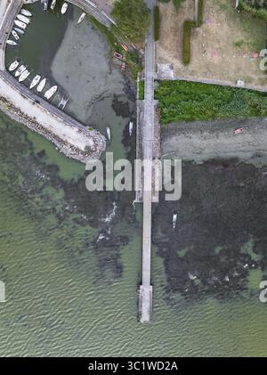 Vue aérienne d'une jetée de pierre s'étendant dans les eaux tranquilles près d'une marina remplie de bateaux, contrastant avec le rivage accidenté, le lac Trasimeno, Ombrie, Italie. Banque D'Images