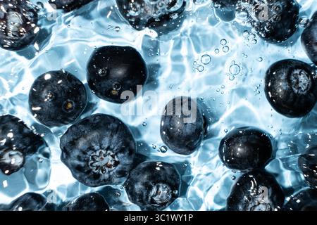Fond de baies de bleuets entiers frais dans l'eau, éclaboussure d'eau, vue de dessus. Banque D'Images