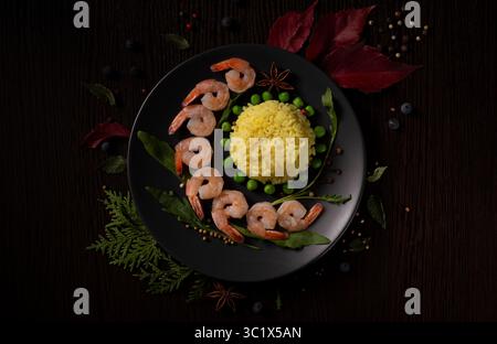 Une assiette magnifiquement stylisée de crevettes et de riz est agencée habilement sur une assiette noire sombre. Le plat comporte un monticule de riz jaune vif, entouré Banque D'Images