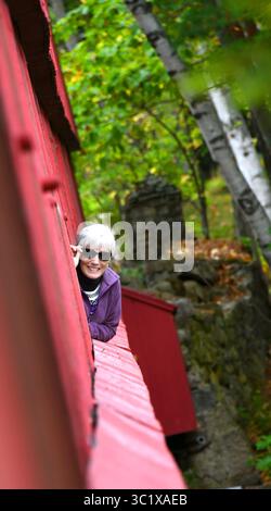 Une femme âgée regarde par une fenêtre du pont couvert de la rivière Swift, Conway, New Hampshire. Elle sourit, a les cheveux blancs et porte des lunettes de soleil Banque D'Images