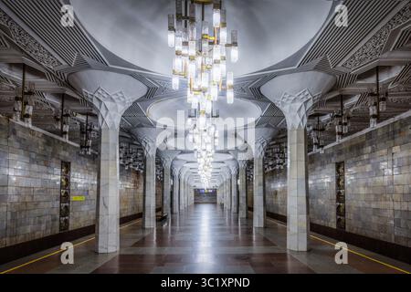 Tachkent, Ouzbékistan - 05 avril 2024 : vue de la station de métro Alisher Navoi, où des colonnes ornées s'élèvent pour rencontrer un plafond à motifs géométriques, illuminé par une série de lustres modernes. Banque D'Images