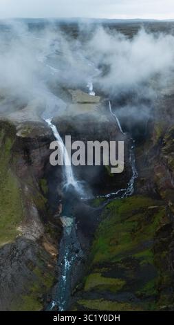 La cascade de Haifoss coule le long de falaises spectaculaires, entourées de verdure luxuriante et de nuages brumeux en Islande. L'eau en cascade crée une atmosphère sereine au milieu de la beauté sauvage de la nature. Banque D'Images