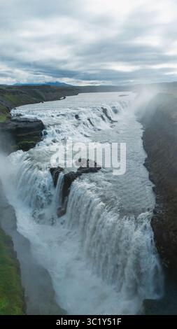 Admirez la vue époustouflante des cascades Gullfoss qui coulent sur les falaises rocheuses, entourées d'une végétation luxuriante et de paysages spectaculaires en Islande. La beauté naturelle captive sous tous les angles. Banque D'Images