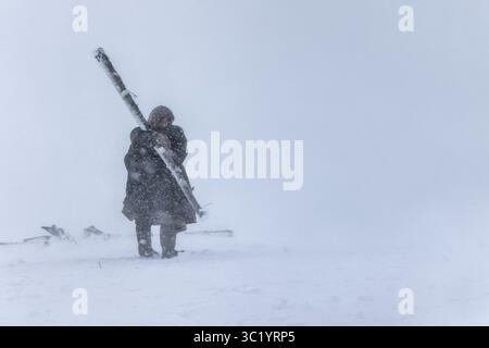 Yamalo Nenets, Russie - 16 avril 2021 : vue d'une figure solitaire combattant le blizzard, une silhouette sombre contre l'étendue blanche aveuglante de neige, portant des poteaux en bois. Banque D'Images