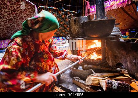 Yamalo Nenets, Russie - 16 avril 2021 : vue d'une femme âgée qui s'occupe d'un poêle à bois, sa lueur ardente illuminant son visage et l'intérieur rustique environnant. Banque D'Images