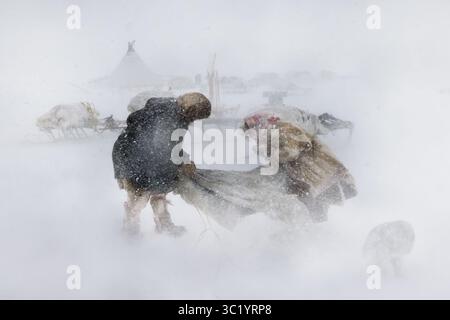 Yamalo Nenets, Russie - 16 avril 2021 : vue de personnages luttant contre le blizzard féroce au milieu d'un paysage de yourtes enneigées et de formes indistinctes. Banque D'Images