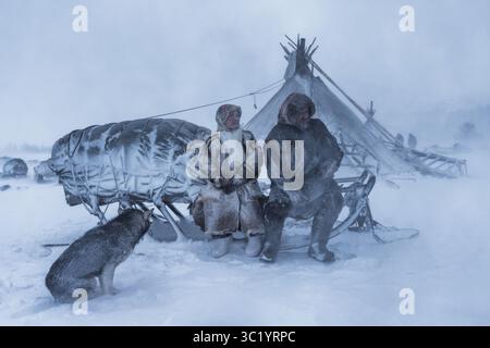Yamalo Nenets, Russie - 16 avril 2021 : vue de peuples indigènes bravant le blizzard en tenue traditionnelle près d'une habitation enneigée, leurs visages gravés avec résilience. Banque D'Images