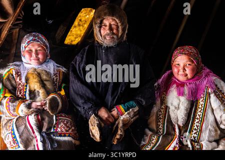 Yamalo Nenets, Russie - 16 avril 2021 : vue de trois personnes en vêtements traditionnels, leurs visages illuminés contre l'intérieur sombre, mettant en valeur les textures de la fourrure et des tissus à motifs. Banque D'Images