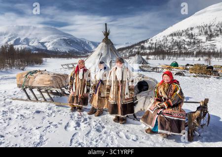 Yamalo Nenets, Russie - 16 avril 2021 : vue de femmes autochtones debout fièrement près de leurs habitations traditionnelles sur fond de sn blanc Banque D'Images