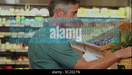 Homme en chemise verte tenant un cahier en spirale examinant l'ananas dans l'allée des fruits et légumes, avec des bacs en bois Banque D'Images