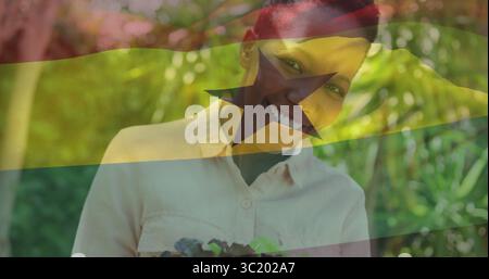 Debout dans le jardin ensoleillé, femme tenant caisse de verts portant chemise avec recouvrement de drapeau Ghana Banque D'Images