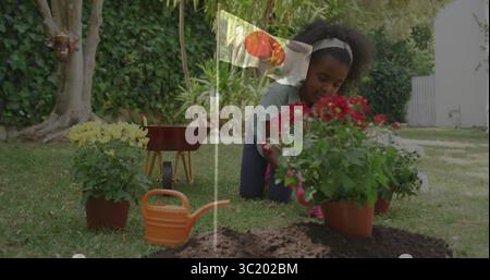 Fille agenouillée plantant des fleurs rouges dans le jardin de l'arrière-cour, avec arrosoir orange et brouette rouge Banque D'Images