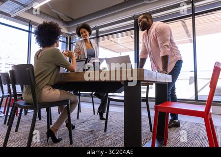 Divers collègues discutent des plans de projet autour de la table dans le bureau avec des ordinateurs portables et une tasse à café Banque D'Images