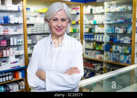 Pharmacien principal en blouse de laboratoire organisant les boîtes de médicaments sur les étagères derrière le comptoir en verre de la pharmacie Banque D'Images