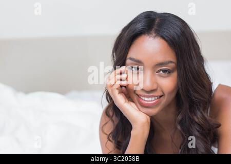 Femme afro-américaine s'inclinant sur le lit à la maison portant haut sans manches avec literie, espace copie Banque D'Images